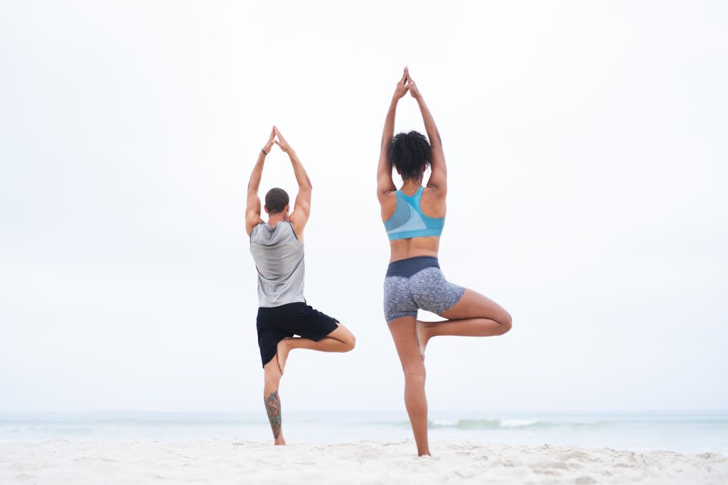 man & woman on beach doing tree pose, healthy, wellness, peace